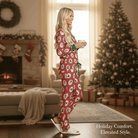 Woman in KRIS KRINGLE KOZY Pajama Set enjoying a cozy holiday moment with a mug by the Christmas tree.