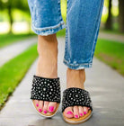 Corkys Bail Money sandals in black with studs, showcasing stylish comfort on a woman walking on a path.