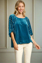 Woman wearing Umgee teal top with velvet lantern sleeves and pearl accents, showcasing stylish high low hem design.