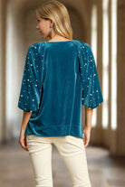 Woman wearing teal velvet top with pearl-detailed lantern sleeves and high low hem by Umgee, shown from the back.