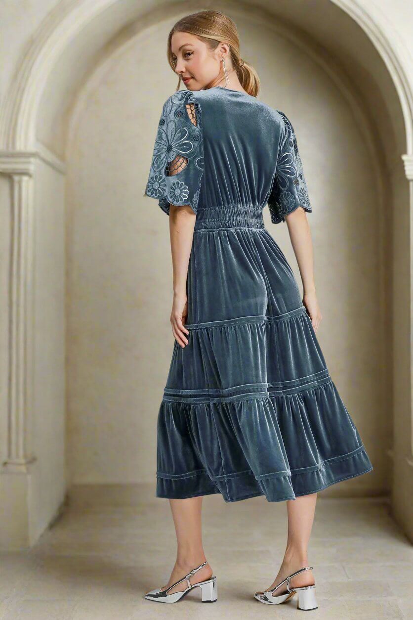 Woman wearing Umgee PURE HAPPINESS Dress with floral lace sleeves in slate blue velvet, showing back view in elegant setting.