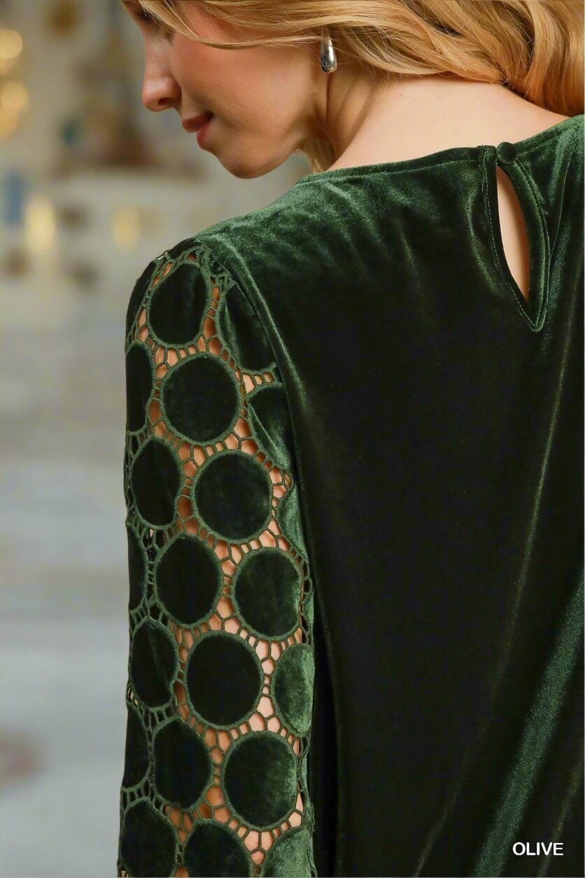 Woman wearing green velvet top with lace polka dot sleeves and keyhole button closure, showcasing elegant holiday fashion.