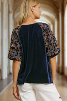 Navy blue velvet top with floral lace poof sleeves worn by a woman, showcasing elegant style and luxurious fabric in a corridor setting.