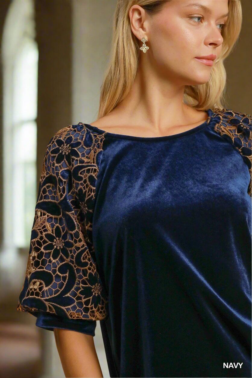 Woman wearing navy blue velvet top with floral lace poof sleeves, showcasing elegant and sophisticated style.