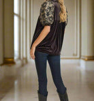 Woman modeling dark velvet top with jacquard embroidery and bubble sleeves by Umgee, paired with jeans and boots.