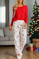 Woman wearing Sweet Dreams Candy Cane Pajamas by a Christmas tree, featuring a red top and candy cane print pants.