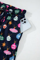 Festive Christmas pajama pants with colorful ornaments, featuring a drawstring waist and pocket with a smartphone peeking out.