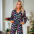 Woman wearing festive holiday pajamas with colorful decorations, standing in a cozy room with Christmas decor.