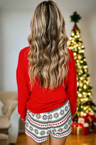 Woman wearing festive SLEIGH GIRL SLEIGH PJ set with snowflake print shorts in front of a Christmas tree.