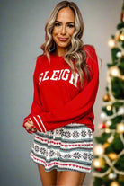 Woman wearing SLEIGH GIRL SLEIGH PJ set with snowflake print shorts, festive Christmas tree in the background.