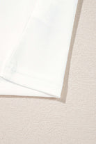 Close-up of the hem and fabric texture of a soft white shirt on a light textured background.