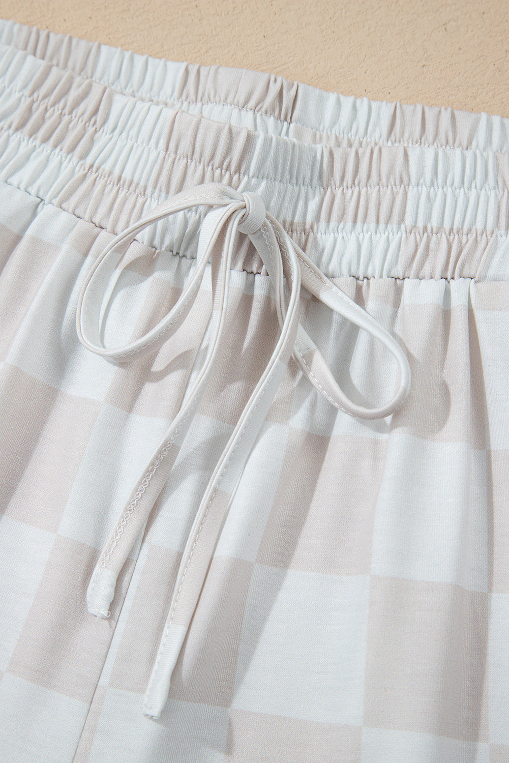 Close-up of drawstring and waistband of checkered two-piece lounge shorts set in neutral tones.