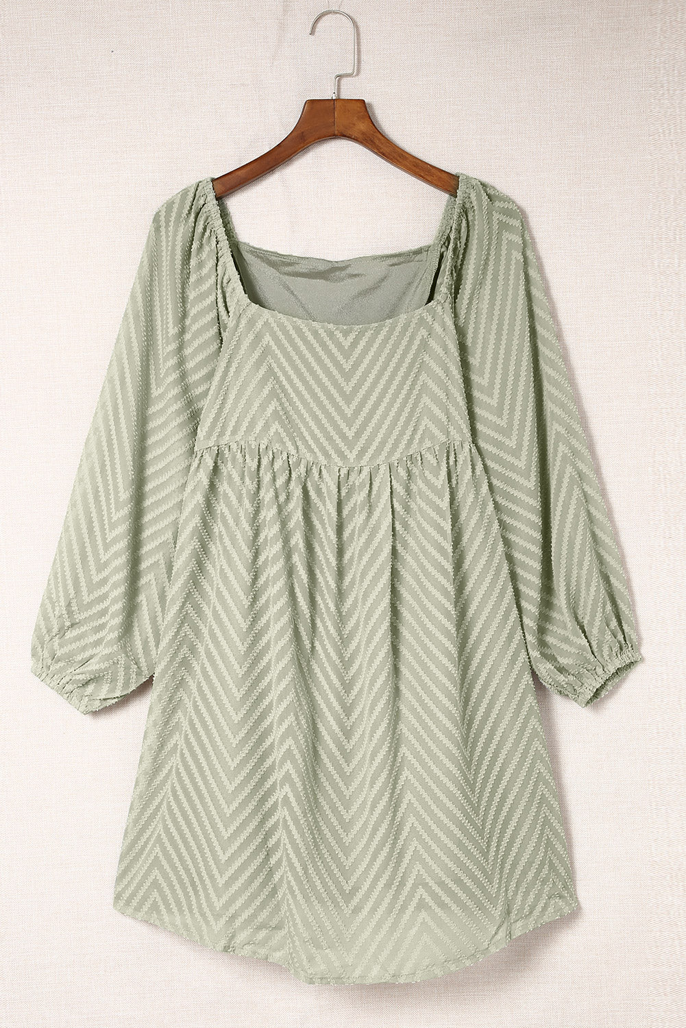 Sage green dress with square neckline, puffed sleeves, chevron pattern, and babydoll style on wooden hanger.