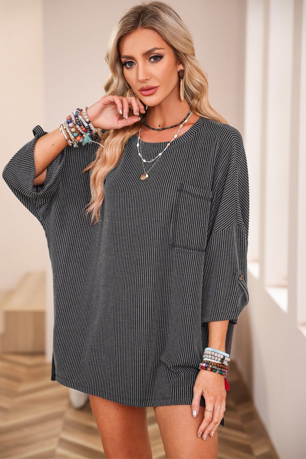 Woman wearing charcoal Lines Drawn Top with ribbed fabric, roll-tab sleeves, and chest pocket, showcasing casual fashion style.