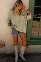 Woman wearing Lines Drawn Top in sage with denim shorts and boots, showcasing ribbed knit fabric and roll-tab sleeves in a stylish pose.