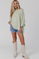 Woman in sage oversized Lines Drawn Top with denim shorts and cream boots, showcasing fashion-forward and comfortable style.