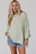 Woman wearing sage oversized ribbed knit top with roll-tab sleeves and chest pocket, paired with blue shorts.