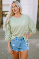 Woman wearing a sage-colored oversized ribbed knit top with roll-tab sleeves, paired with distressed denim shorts.