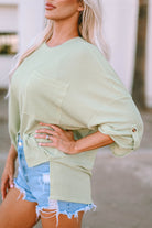 Woman wearing Lines Drawn sage top with ribbed fabric and roll-tab sleeves, paired with denim shorts, showcasing a casual style.