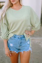 Sage oversized knit top with roll-tab sleeves and chest pocket paired with distressed denim shorts.