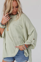 Woman wearing sage ribbed knit oversized top with roll-tab sleeves, chest pocket, and colorful bracelets, paired with denim shorts.