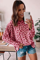 Woman wearing pink leopard print long sleeve top with relaxed fit, styled with denim shorts and smiling in a cozy setting.