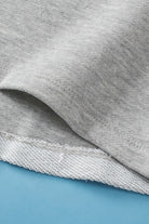 Close-up of gray knit fabric showing texture and hem detail of Read Between the Lines Top by Vivian-Lu against blue background.