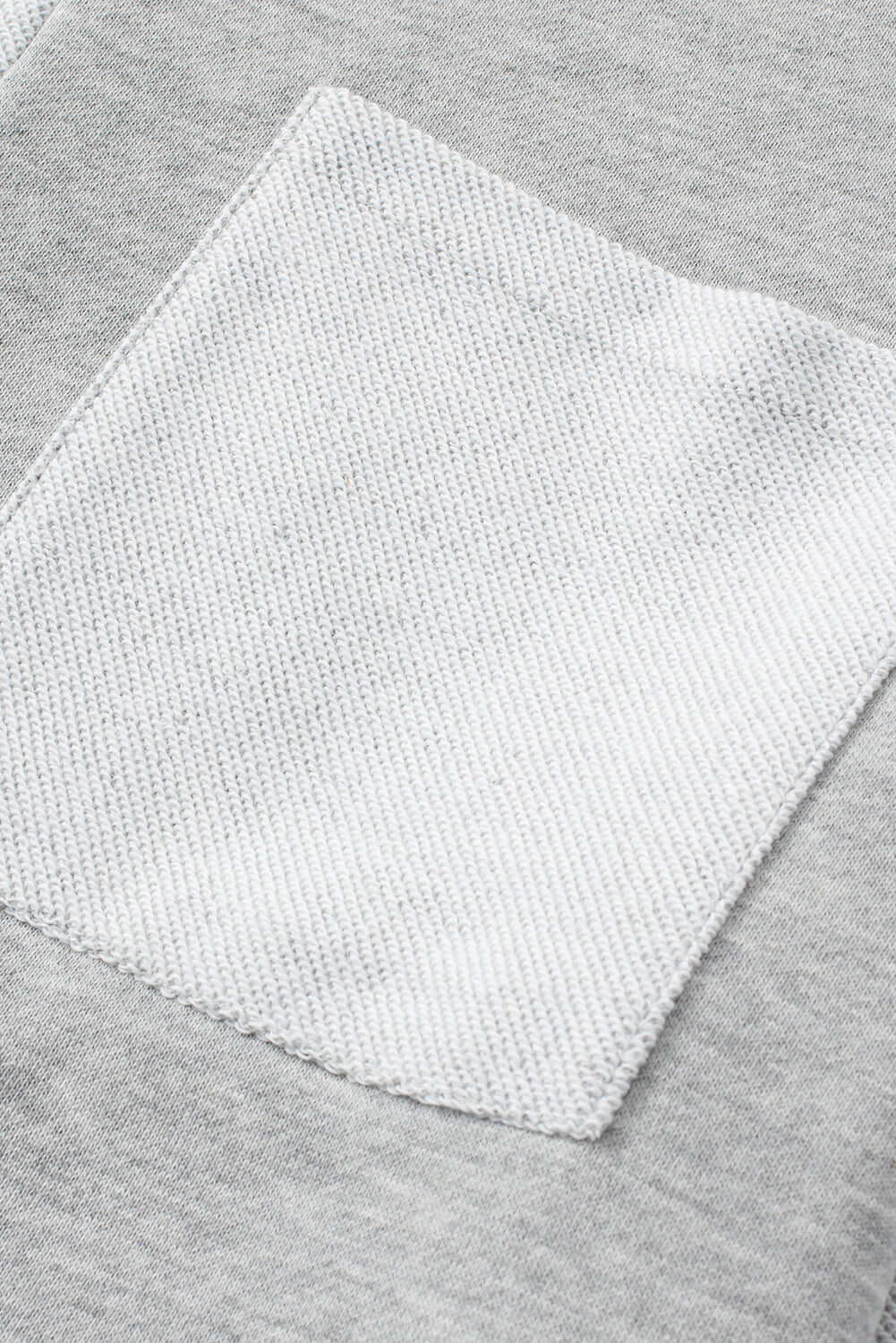 Close-up of chest pocket on READ BETWEEN THE LINES knit top by Vivian-Lu, featuring a contrasting patchwork design in grey tones.