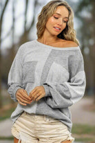 Woman wearing a grey knit top with patchwork design and chest pockets, paired with casual shorts, showcasing relaxed fashion style.