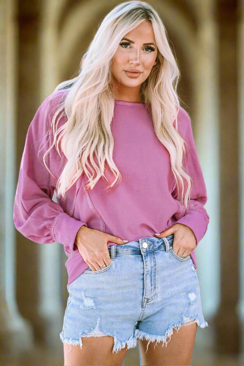 Stylish woman in a pink top and denim shorts, featuring exposed seam detailing for a trendy look.