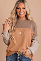 Woman wearing taupe and tan color block top with ribbed texture and long sleeves, paired with jeans and layered necklaces.