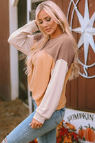 Woman wearing a STANDOUT Color Block Top in taupe and tan with long sleeves, standing outdoors near a rustic barn wall.