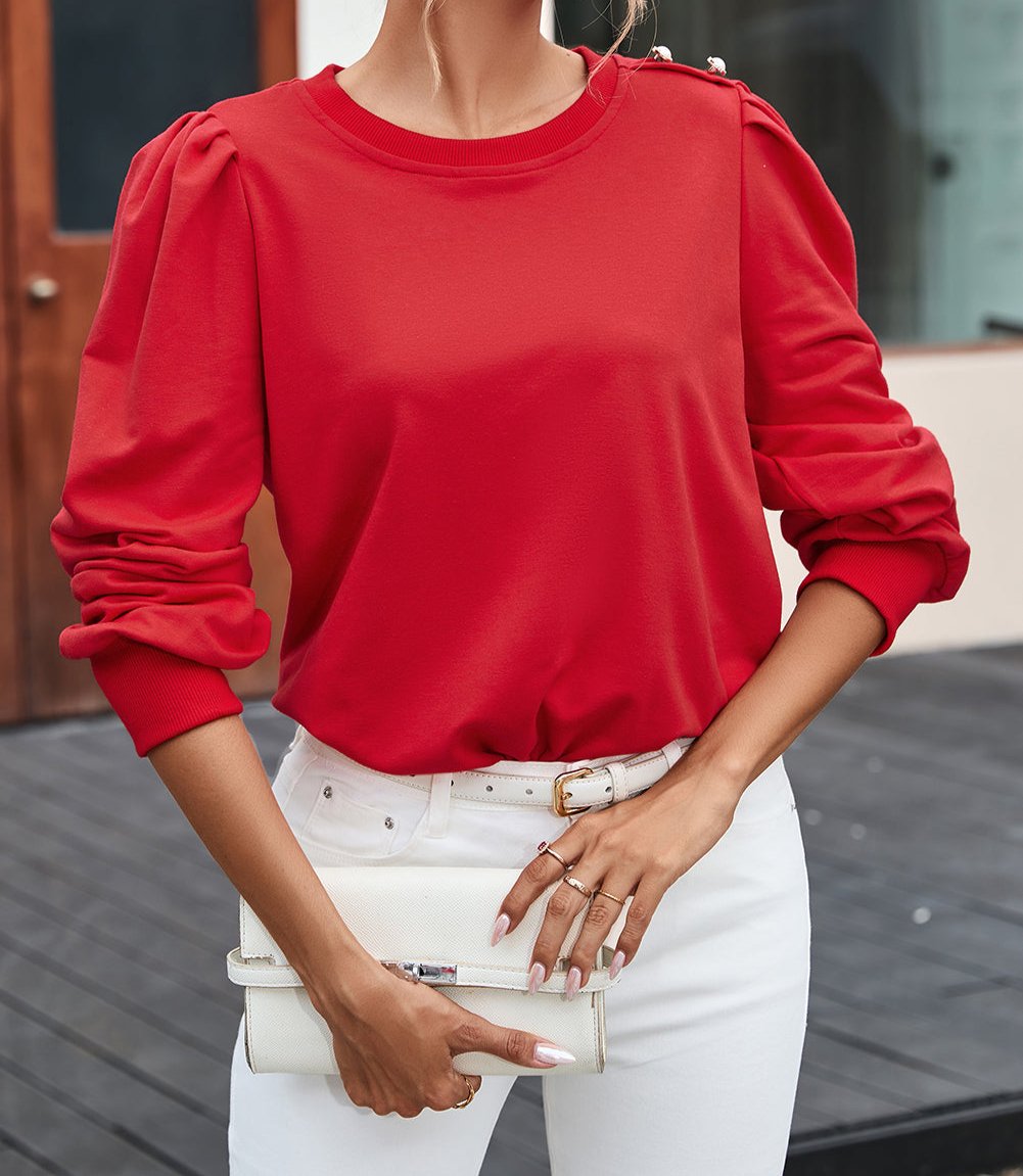 Woman wearing a stylish red top with Bishop sleeves and round neck, paired with white pants and a clutch, perfect for fall fashion.