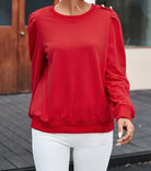 Woman wearing LADY IN RED TOP with Bishop sleeves and button-tab detail, paired with white pants for a chic fall look.