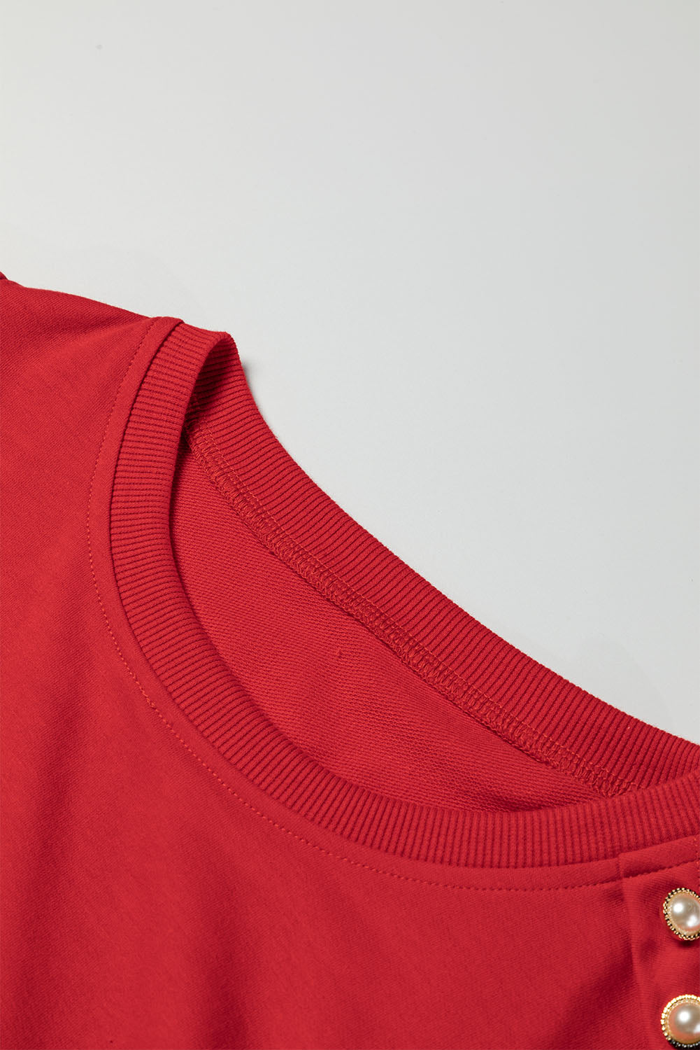 Close-up of LADY IN RED TOP highlighting the round neck and elegant button-tab detail.