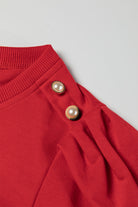 Elegant red top with delicate button-tab detail and bishop sleeves, perfect for fall fashion.