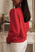 Woman wearing red top with Bishop sleeves, side view, styled with white pants and statement earrings, elegant fall and winter fashion.