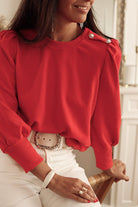 Woman wearing a LADY IN RED TOP with Bishop sleeves and button-tab detail, styled elegantly with white pants, ideal for fall and winter.