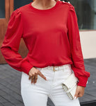 Woman wearing Lady in Red top with Bishop sleeves and button-tab detail, paired with white jeans and a clutch handbag.