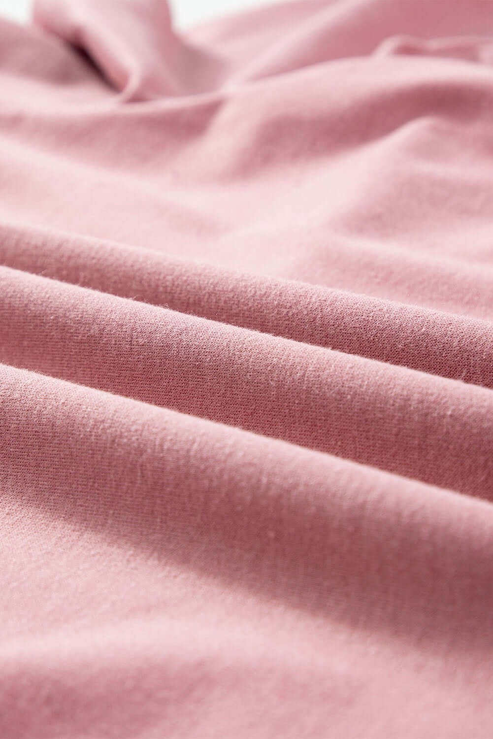 Soft pink fabric texture close-up with gentle folds, showcasing material used in the Rose by Any Other Name Top.