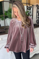 Woman wearing Lilac Luxe Top in soft velvet with pleated round neck, long sleeves, and keyhole back, styled with a pearl necklace.