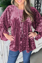 Woman wearing rose pink Velvet Whisper blouse with ruffled pagoda sleeves and a pearl necklace, showcasing soft crushed velvet material.