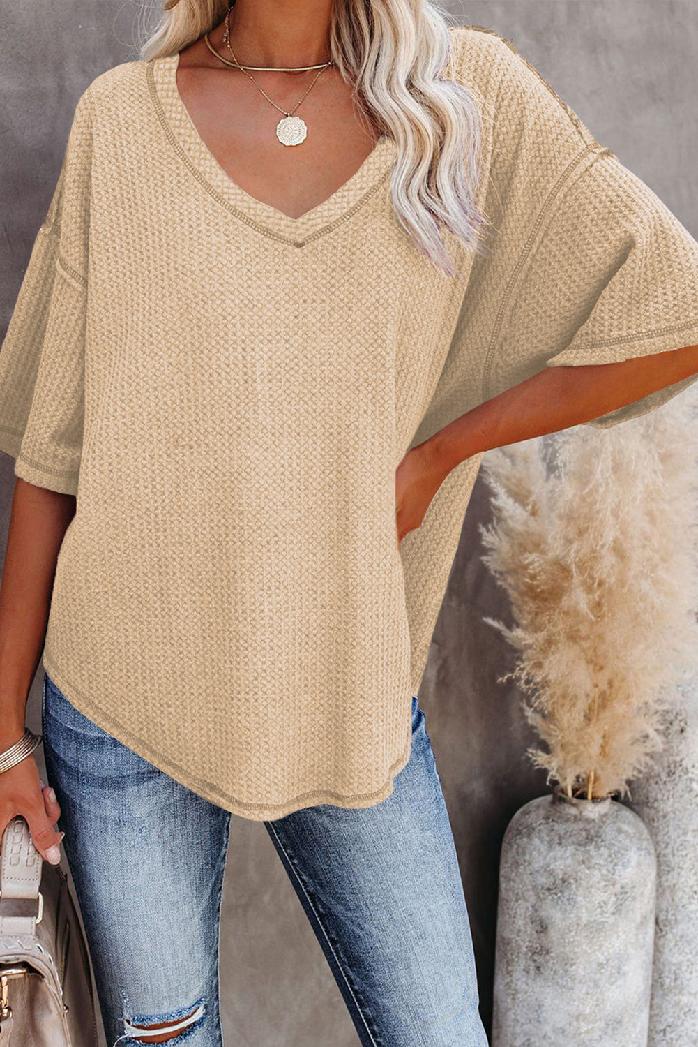 Woman wearing a relaxed cream knit top with V-neck and half sleeves, styled with jeans.