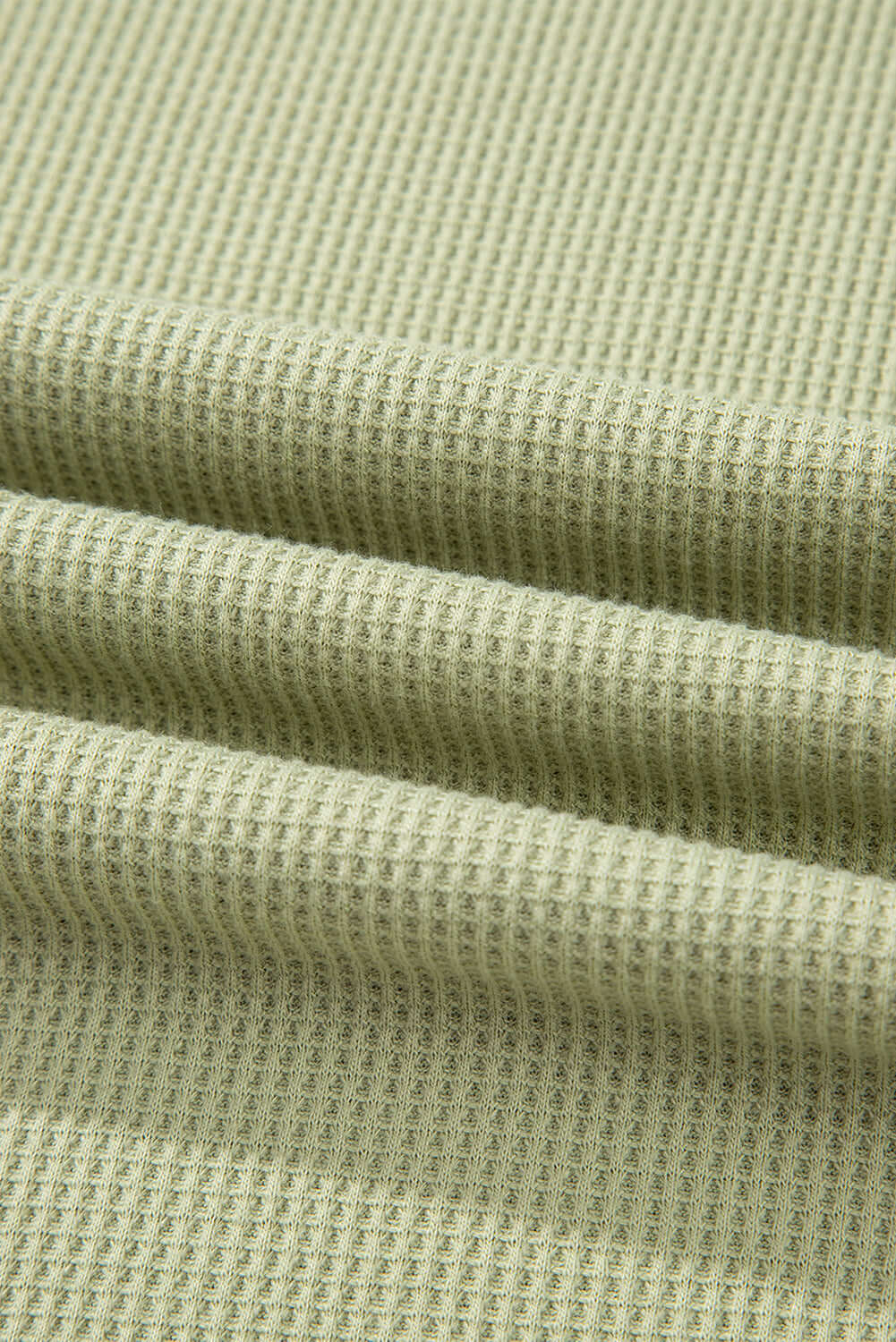 Close-up of textured sage green fabric, showcasing soft, breathable knit for casual summer wear.