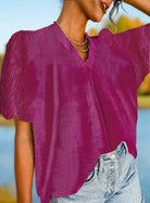 Woman wearing Raspberry Gemtone Top with short bubble sleeves, pleated texture, and V-neckline, paired with denim jeans.