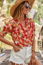 Model wearing Tropical Tango red floral blouse with bubble sleeves and shorts, enjoying a sunny outdoor setting.