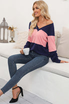 Woman in a pink and navy color-blocked V-neck top, sitting with a cup in hand, styled with skinny jeans and heels.