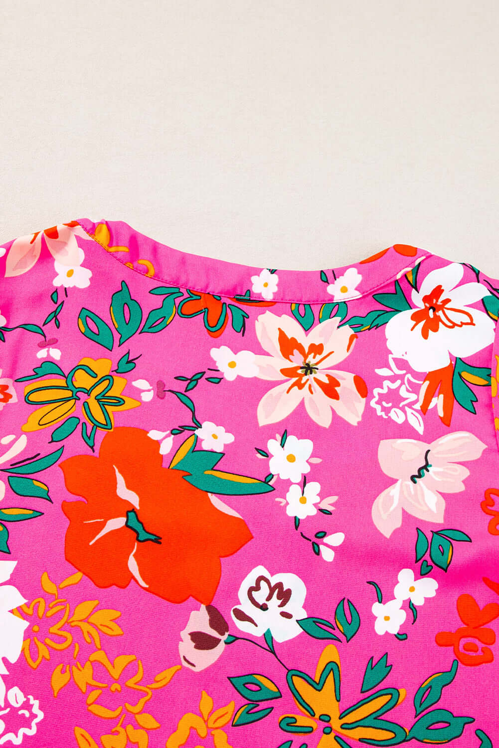 Rose floral print detail on pink blouse with vibrant colors and a split V-neck design.