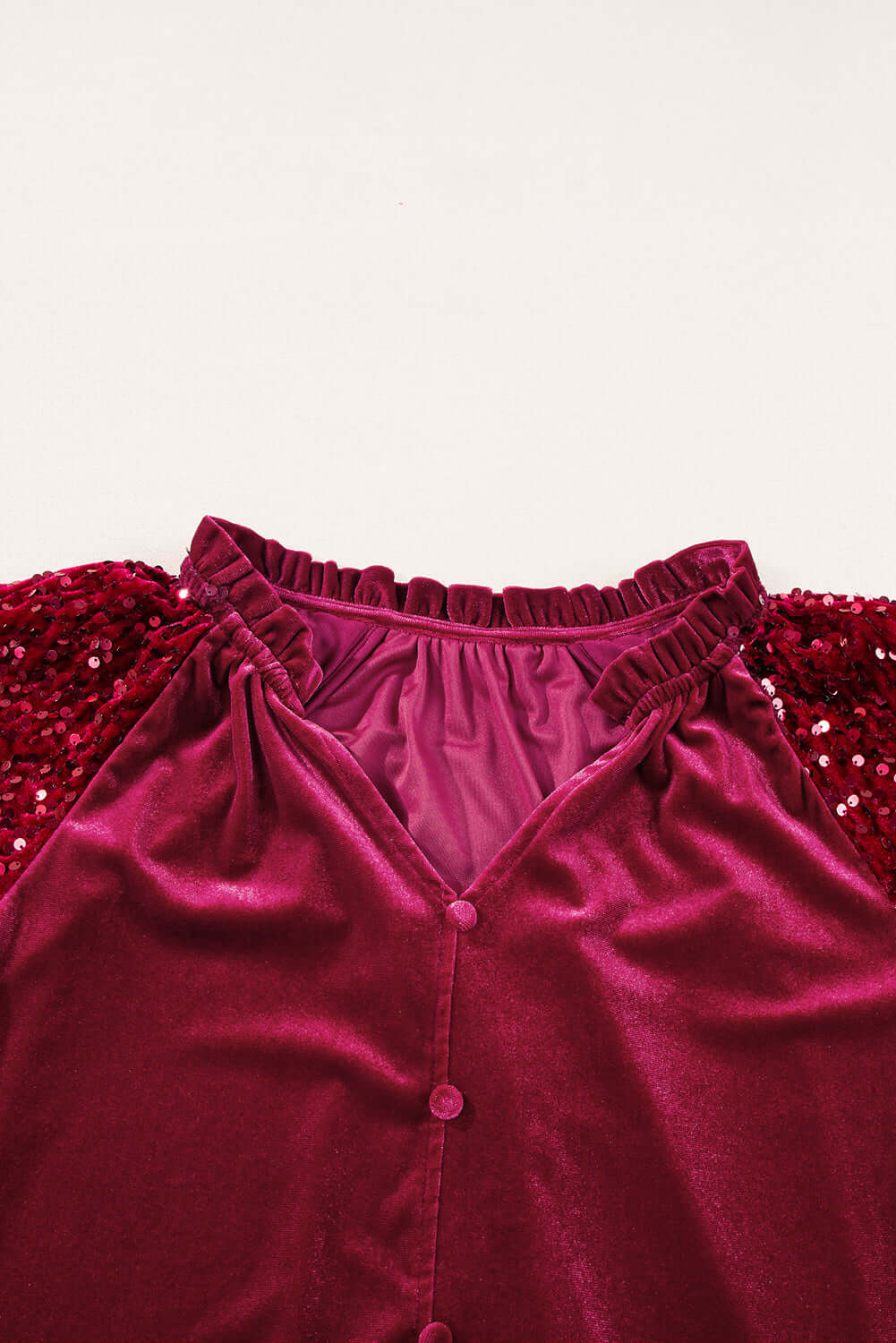 Close-up of SEQUIN SIREN top showcasing the v-cut neckline, ruffle details, and sequined sleeves in rich velvet fabric.