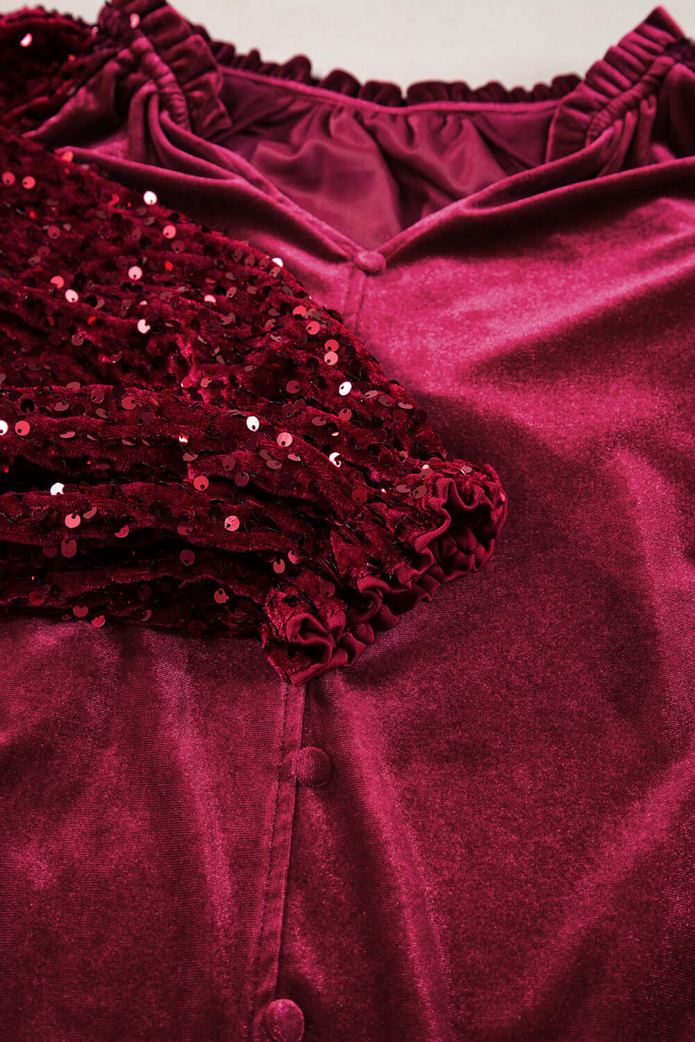 Close-up of SEQUIN SIREN top featuring velvet fabric, ruffled neckline, and sequined sleeves for glamorous holiday fashion.